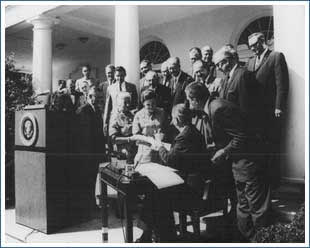 President Lyndon Johnson signs the Wilderness Act of 1964 in the White House Rose Garden. Also pictured are Interior Secretary Stewart Udall, Senator Frank Church, Mardy Murie, Alice Zahniser, and Representative Wayne Aspinall, among others.